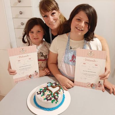 Mutter und Töchter dekorieren kleine Torte mit Fondant